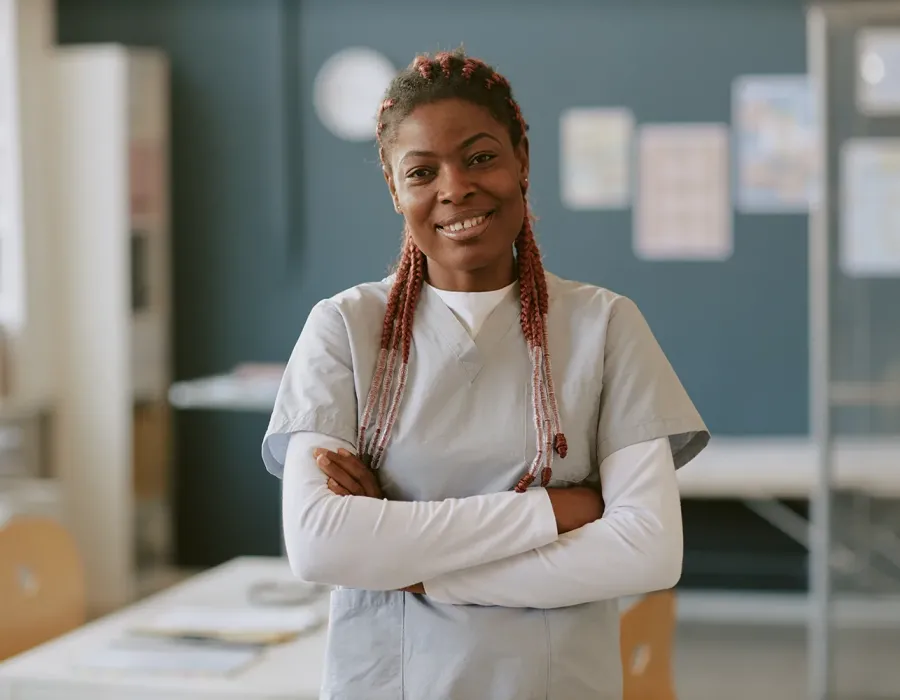Registered nurse smiling with folded arms wearing gray scrubs in medical office